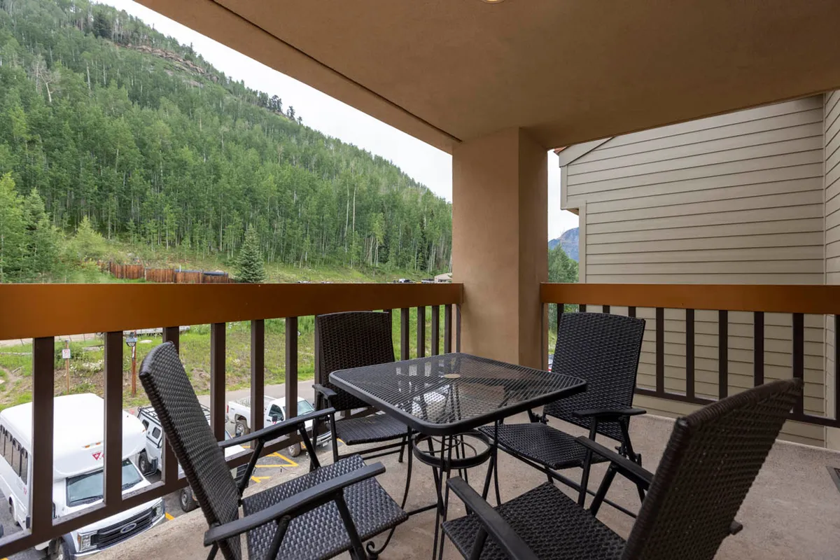 A tranquil balcony scene with a table and chairs overlooking majestic mountain views. The setting suggests a perfect spot for morning coffee, reading, or simply soaking in the natural beauty. The space is inviting and intimate, ideal for couples or solo travelers seeking relaxation and connection with the outdoors.