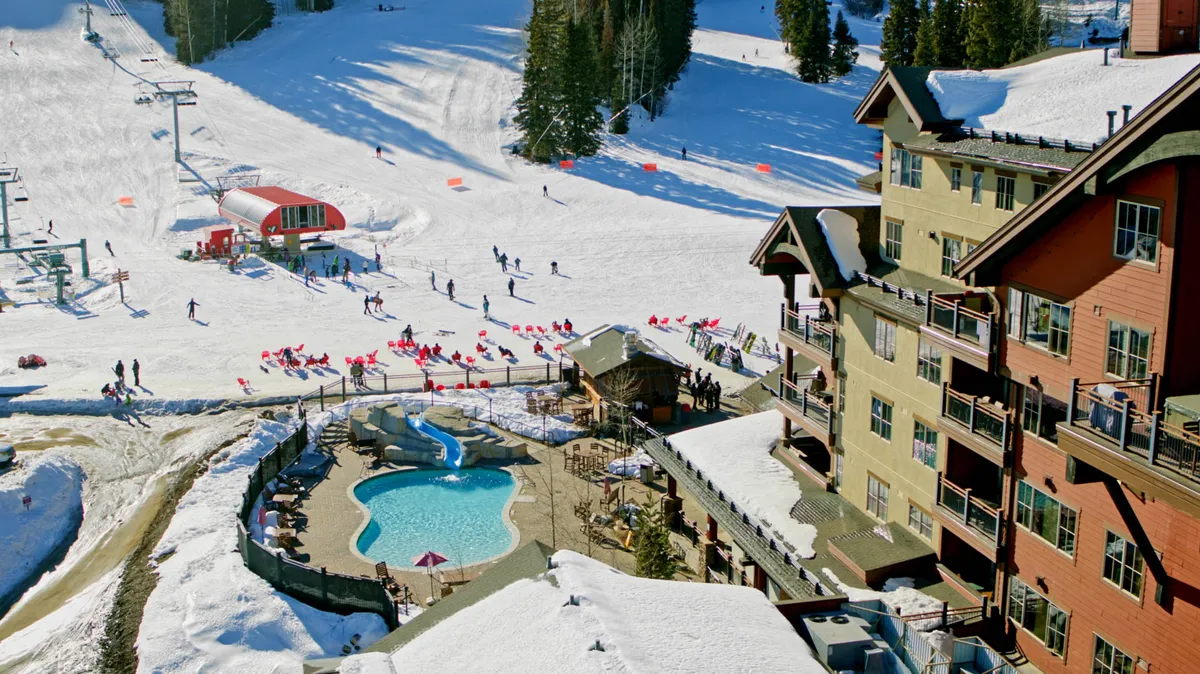 This dynamic exterior image shows the sparkling outdoor pool alongside ski slopes and a ski lift, with the lodge building in the background. It captures the balance between invigorating outdoor activities and relaxing resort amenities—a pool for unwinding after a day on the slopes.