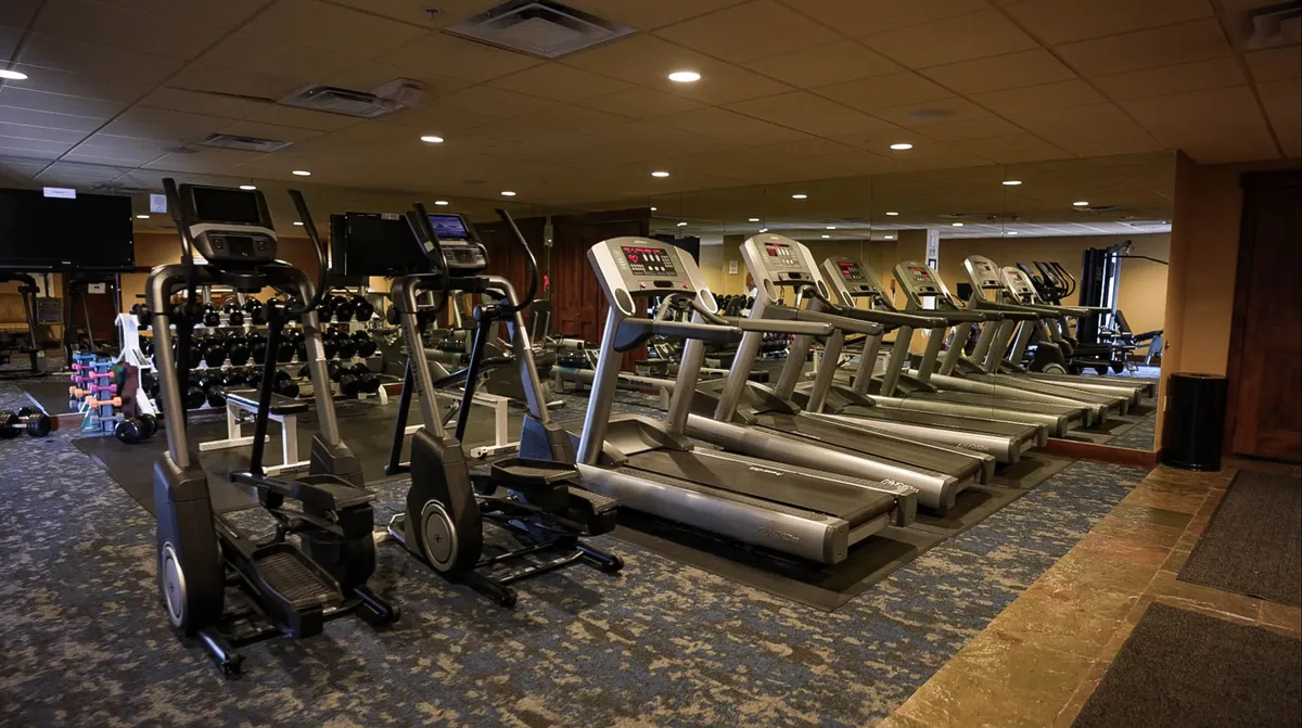 A bright, well-equipped fitness center with treadmills, ellipticals, and dumbbells arranged in an organized, inviting layout. The space feels motivating and ready for personal or group workouts.