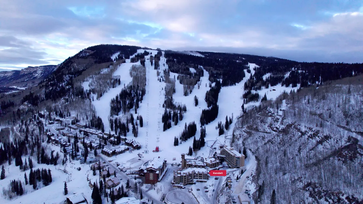 This exterior image captures the snow-covered ski slopes, resort buildings, ski lifts, and trees dusted with fresh powder. The scene buzzes with the energy of skiers and snowboarders, while the resort itself looks inviting and active. The expansive mountain backdrop emphasizes the adventure that awaits right outside the door.